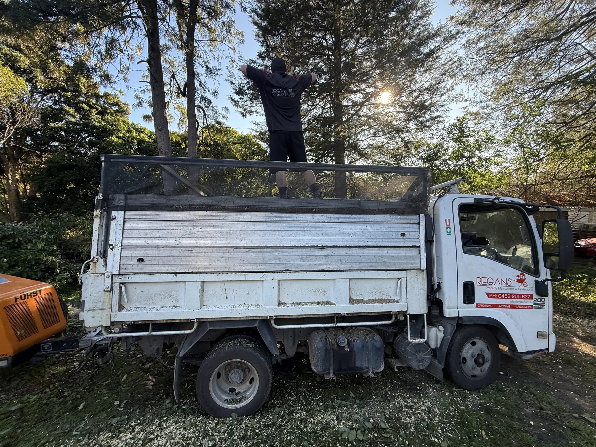 Loading green waste into a Regan's tipper truck beside a wood chipper
